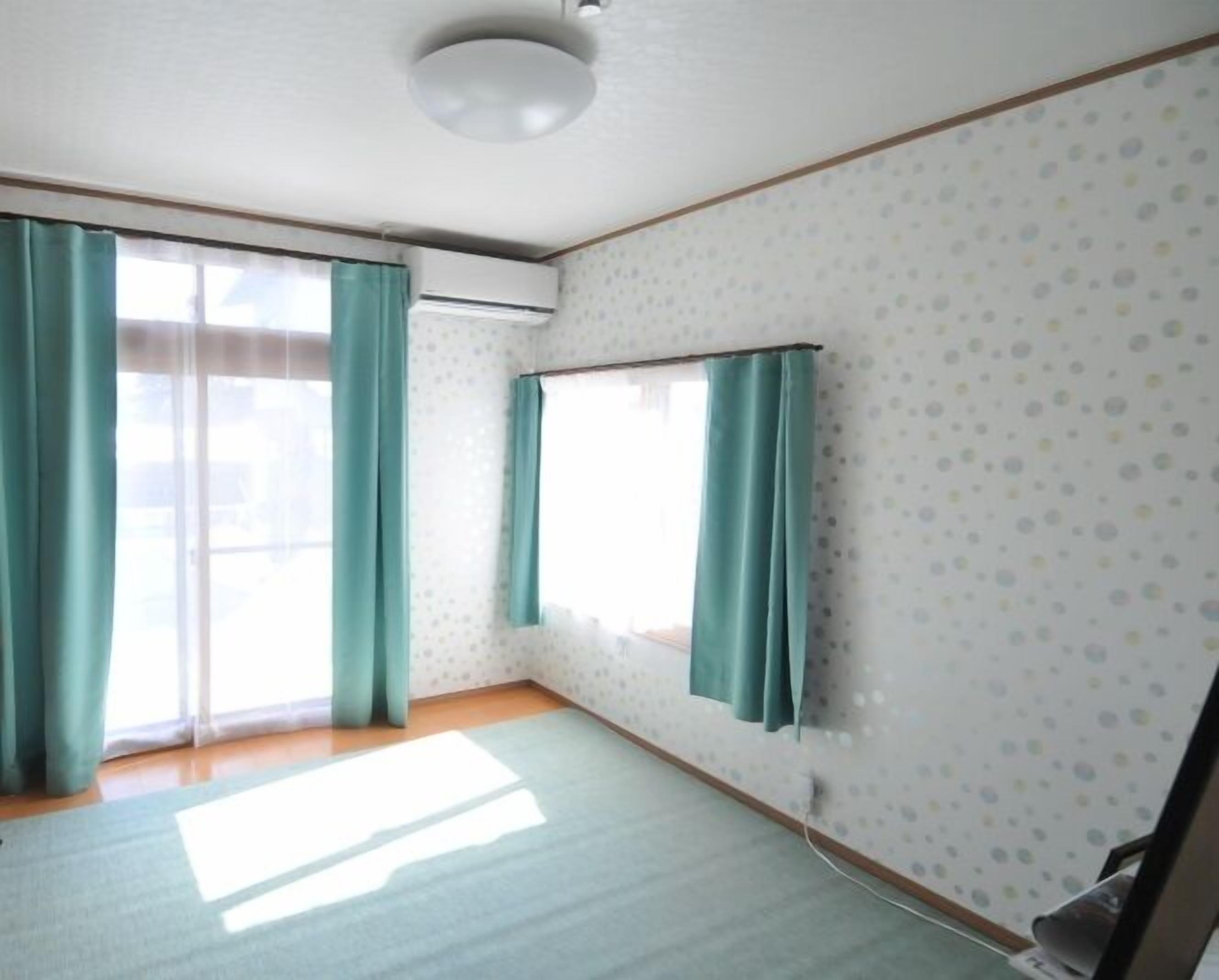 A room with a large window, teal curtains, a wall-mounted air conditioner, and a wooden floor.