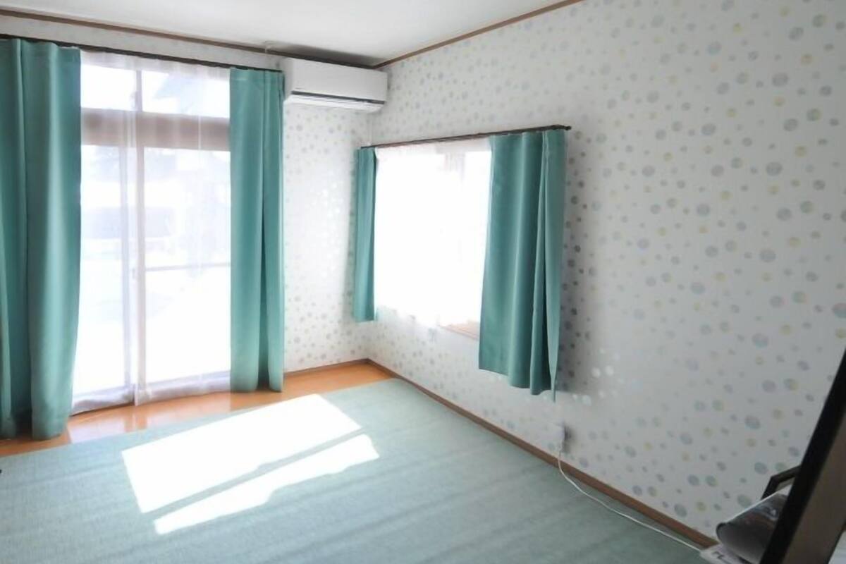 A room with a large window, a wall-mounted air conditioner, and a visible power outlet.