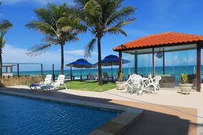 A poolside area with lounge chairs, umbrellas, and a glass-enclosed structure overlooking the ocean.