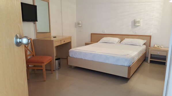A bedroom with a bed, a desk, a chair, a TV mounted on the wall, and a bedside table with a phone.