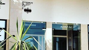 A hotel entrance with a large potted plant in the foreground and a sign above the door. - Hotel El Kssour (Medenine)