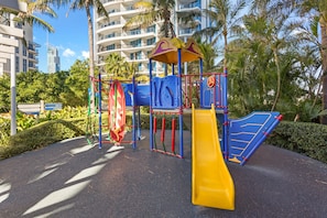 A playground with a yellow slide, blue climbing structures, and a red and green climbing wall.