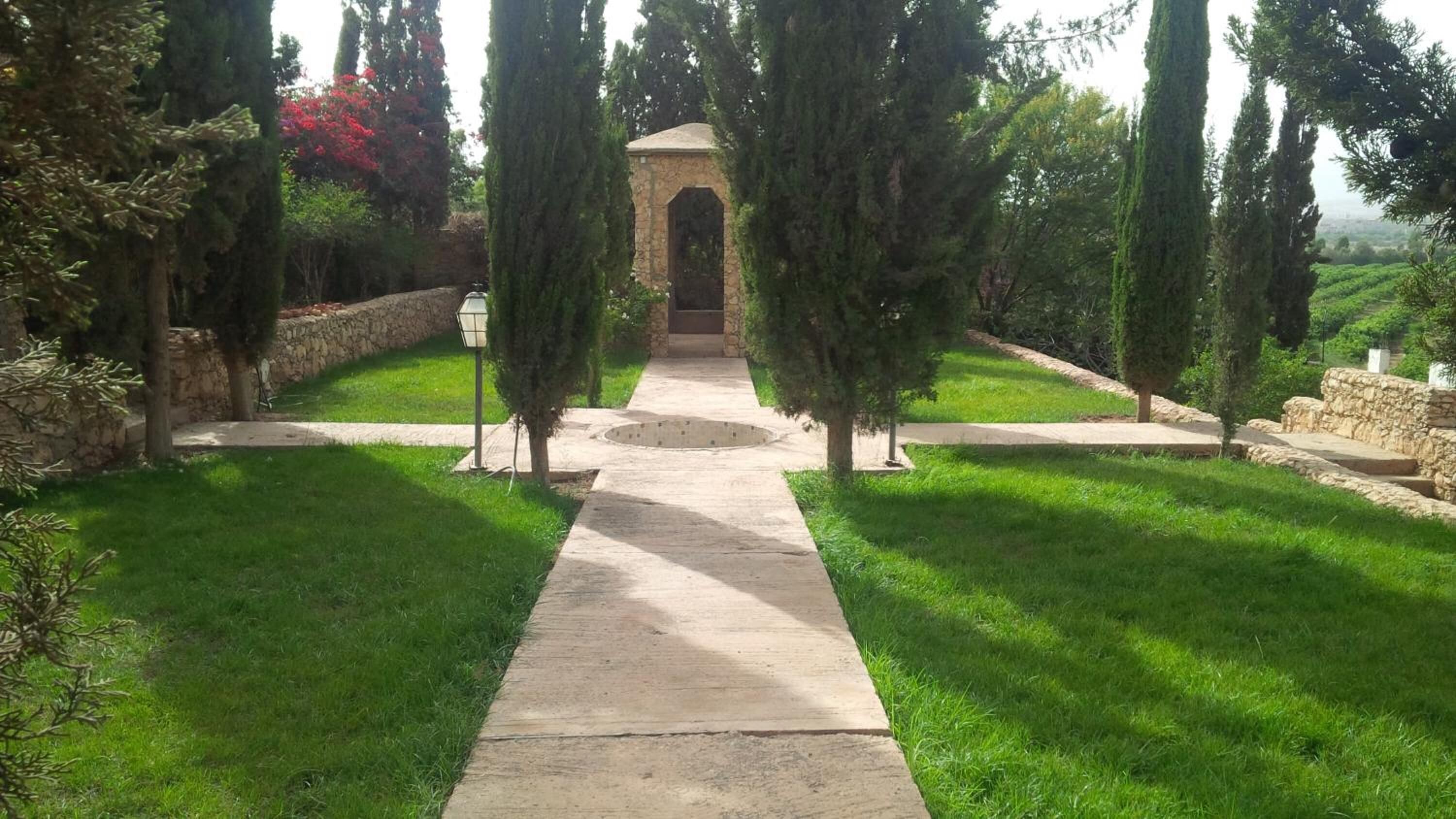 Un sendero conduce a una estructura de piedra con techo abovedado, rodeada de césped cuidado y árboles.