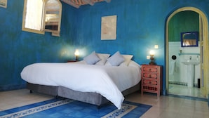 A bedroom with a large bed, two bedside lamps, a mirror, and a bathroom visible through an archway.