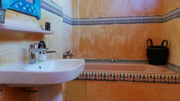 Une salle de bain avec un lavabo blanc, une baignoire et un sac noir posé sur le sol.