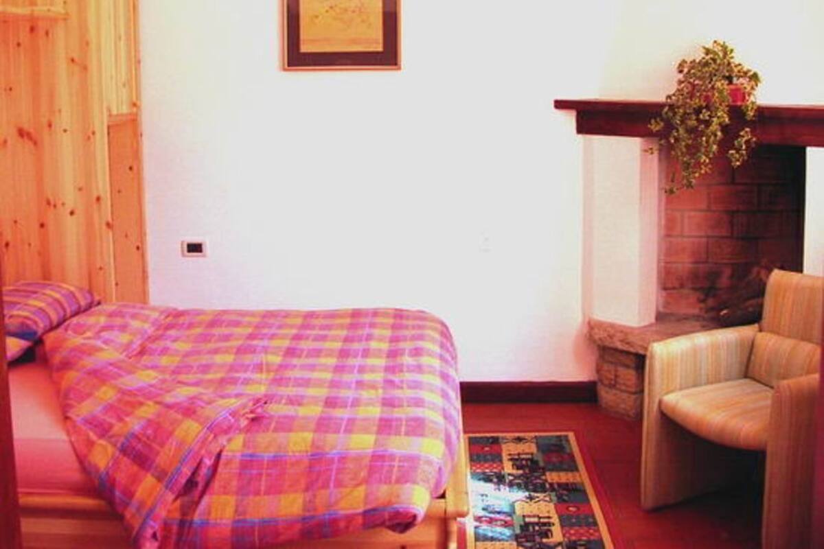 A cozy room with a bed, a chair, a fireplace, and a framed picture on the wall.