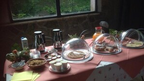 A breakfast table with various food items and condiments, set against a window with a view of greenery. - Agriturismo Ai Gradoni (Teolo)