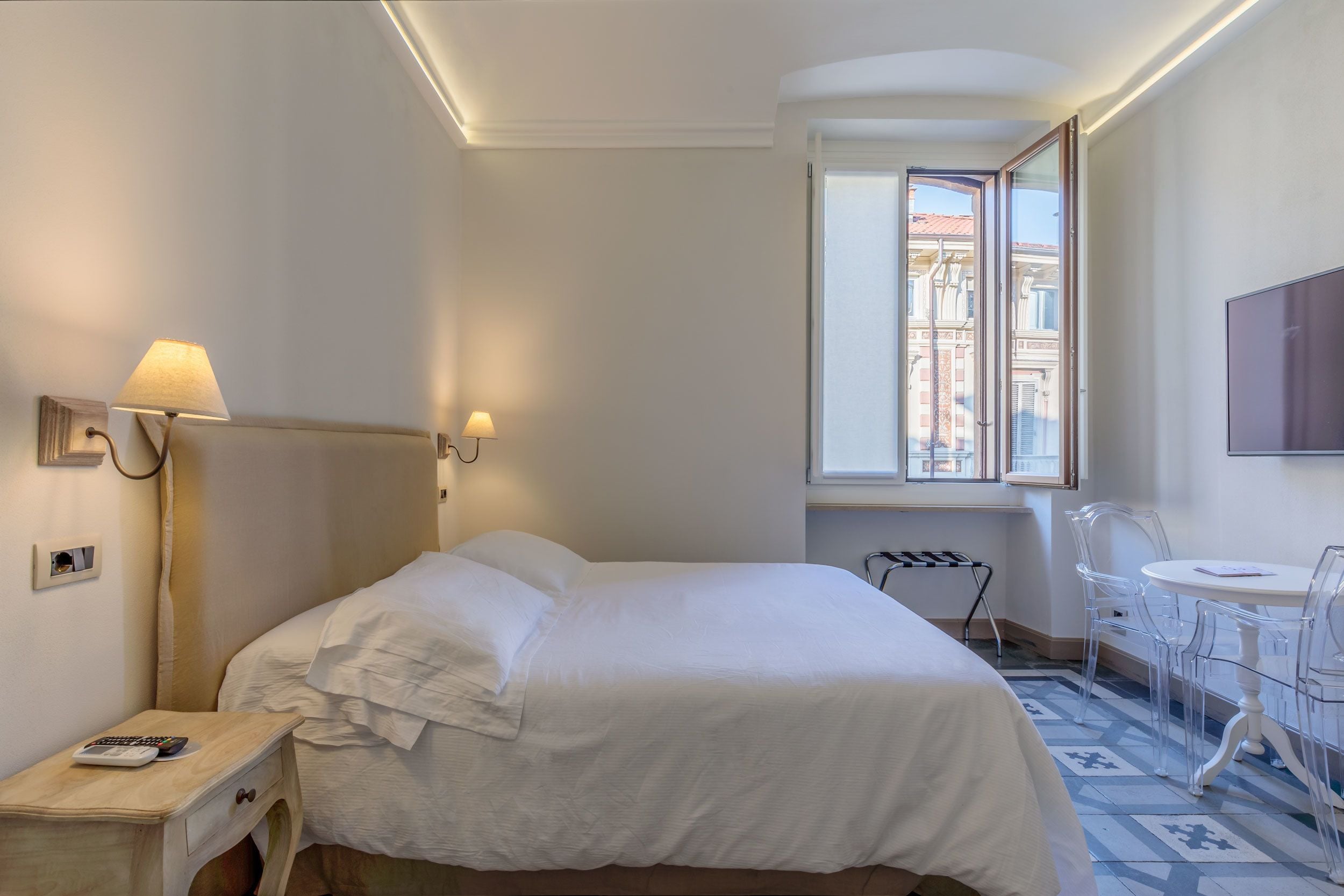 Une chambre d’hôtel comprenant un lit, une table de chevet, une lampe, une fenêtre et une petite table avec des chaises.