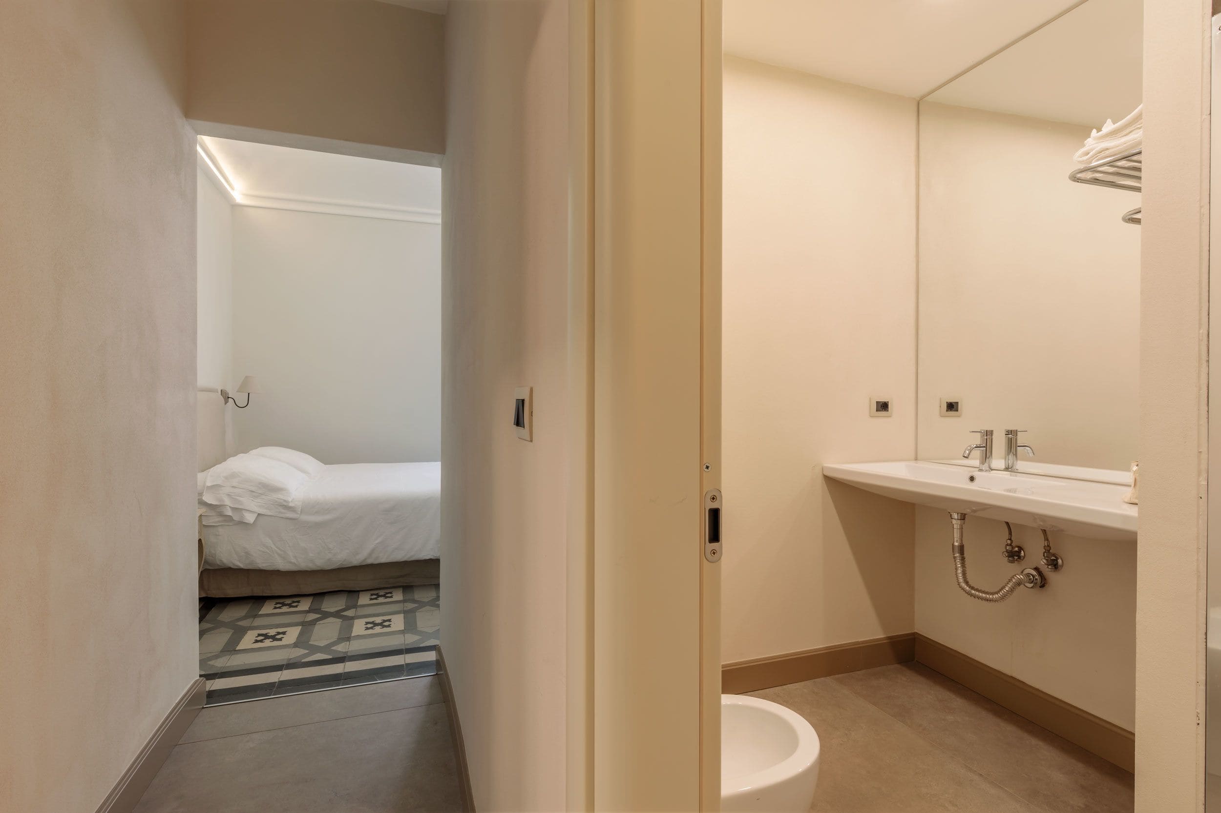 Um banheiro de hotel com pia branca, espelho e vaso sanitário.