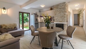 A modern living room with a sofa, a dining table with chairs, and a kitchen area with a stone fireplace. - Villa Irma in Golas, Croatia (Golas)