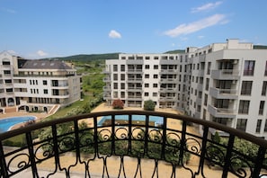 A multi-story hotel with balconies, a swimming pool, and a view of the surrounding landscape.