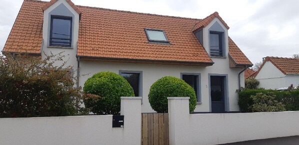Une maison à deux étages, avec un toit recouvert de tuiles rouges, des murs extérieurs blancs et une petite fenêtre au deuxième étage.