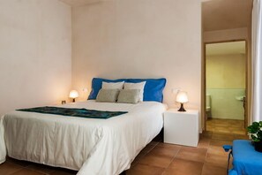 A hotel room with a bed, bedside lamps, a small table with a lamp, and a view of a bathroom. - MARGARITA SAMPOL PALOU Can Selva, village house with fantastic views as far as Pto. Alcudia (SELVA)