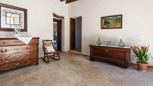A room with a wooden dresser, a chair, a small table with decorative items, and a painting on the wall. - MARGARITA SAMPOL PALOU Can Selva, village house with fantastic views as far as Pto. Alcudia (SELVA)