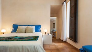 A hotel room with a bed, bedside lamps, a small table, and a view of the hallway. - MARGARITA SAMPOL PALOU Can Selva, village house with fantastic views as far as Pto. Alcudia (SELVA)
