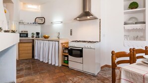 A compact kitchen with a stove, oven, and microwave. There is a wooden chair and a dining table with a white tablecloth. - MARGARITA SAMPOL PALOU Can Selva, village house with fantastic views as far as Pto. Alcudia (SELVA)