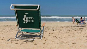 Une chaise de plage portant la marque « Ships Watch », placée sur une plage de sable.