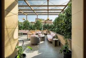 Un espacio al aire libre iluminado por el sol con mobiliario acolchado y plantas en macetas.