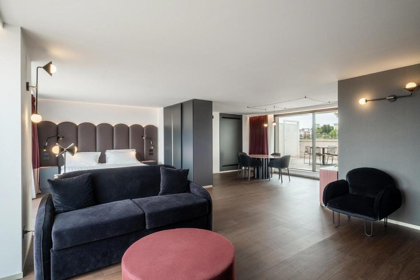 Habitación de hotel moderna con cama, sofá, zona de comedor y vistas a través del ventanal.