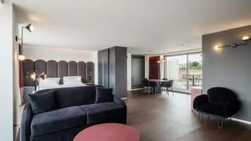 Habitación de hotel moderna con cama, sofá, zona de comedor y vistas a través del ventanal.