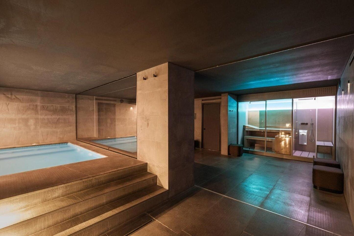 Uma área de spa moderna com uma grande banheira de hidromassagem, sauna e espaço de chuveiro com paredes de vidro.