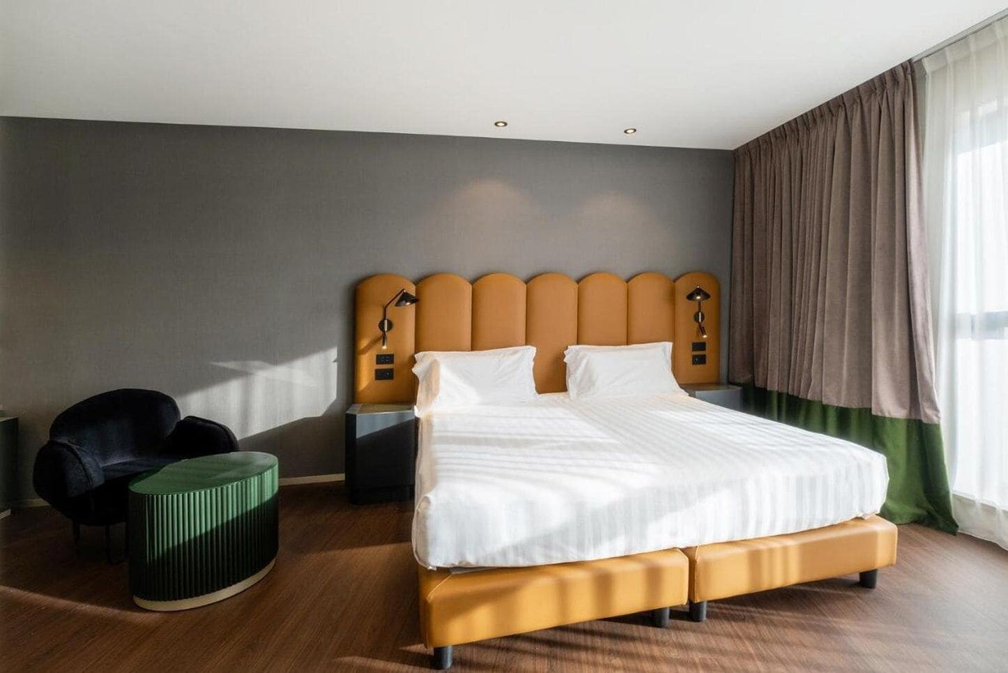 A hotel room with a large bed, a nightstand, a chair, and a window with curtains.