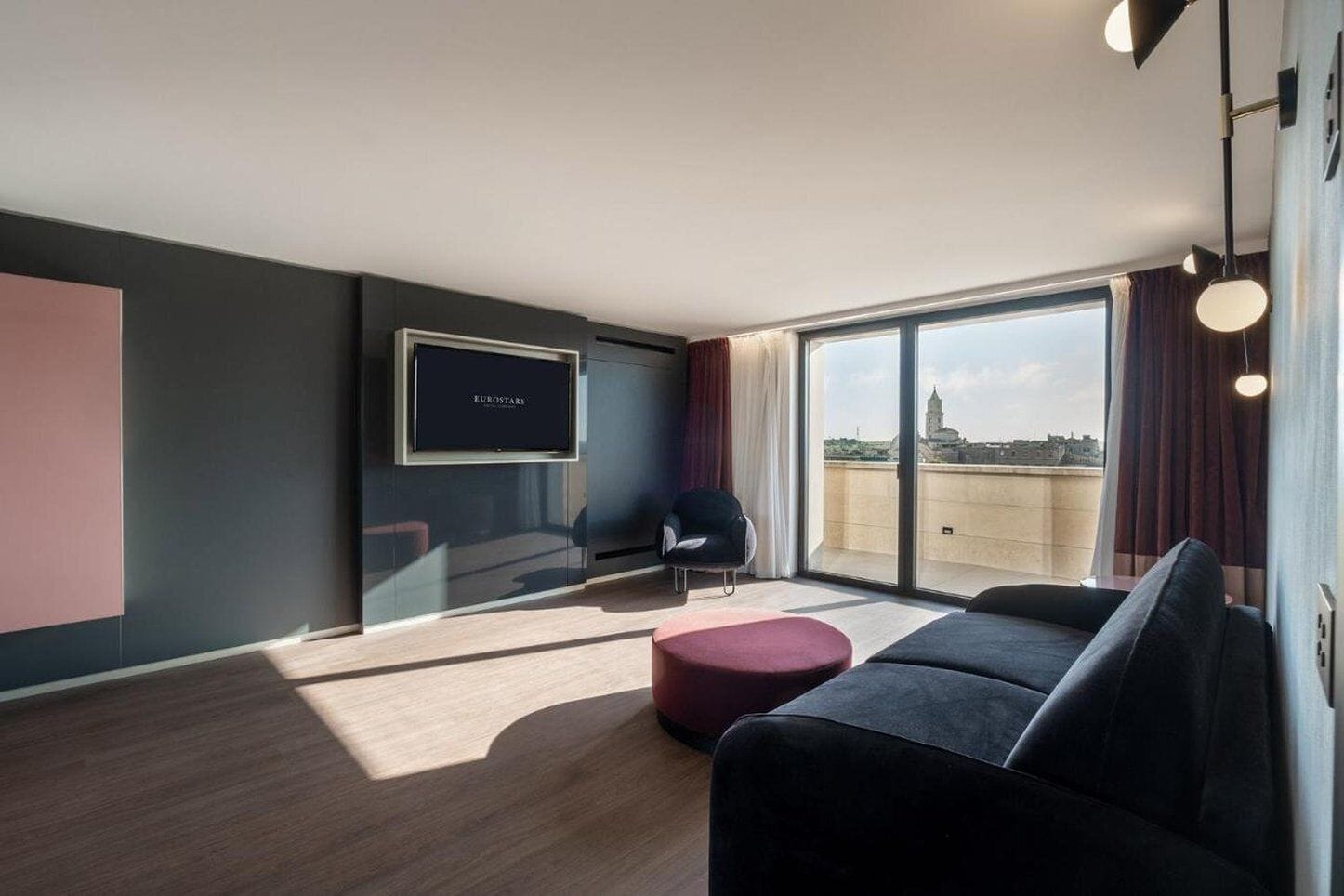 A modern living room with a large window, a flat-screen TV, a sofa, and a chair.