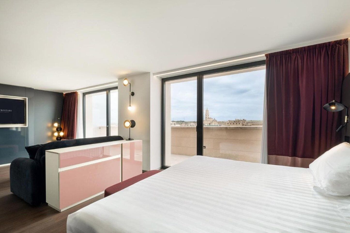 A modern hotel room with a large bed, a desk, and a view of a cityscape.