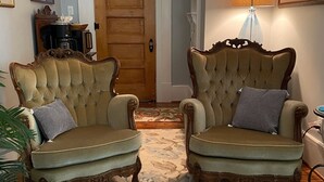 Une pièce comprenant deux fauteuils richement décorés, un tapis à motifs, une porte en bois et une lampe.