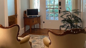 Une pièce comprenant deux fauteuils, un bureau en bois avec un téléviseur, une grande fenêtre avec des vitraux décoratifs et un luminaire au plafond de forme géométrique.