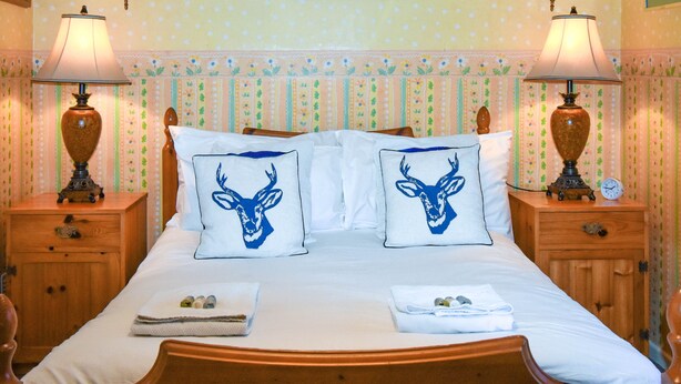 Un lit avec deux oreillers ornés d’un motif de cerf, une table de chevet avec une lampe et une horloge.