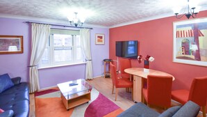 Un salon comprenant un canapé, une table basse, un téléviseur et un coin repas avec des chaises et une table.