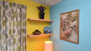 Une pièce avec un mur jaune, un mur d’accent bleu, un tableau encadré, une lampe et une plante posée sur une étagère.