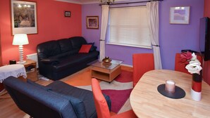 Un salon avec un canapé noir, un fauteuil rouge, une table basse en verre et une table à manger en bois.