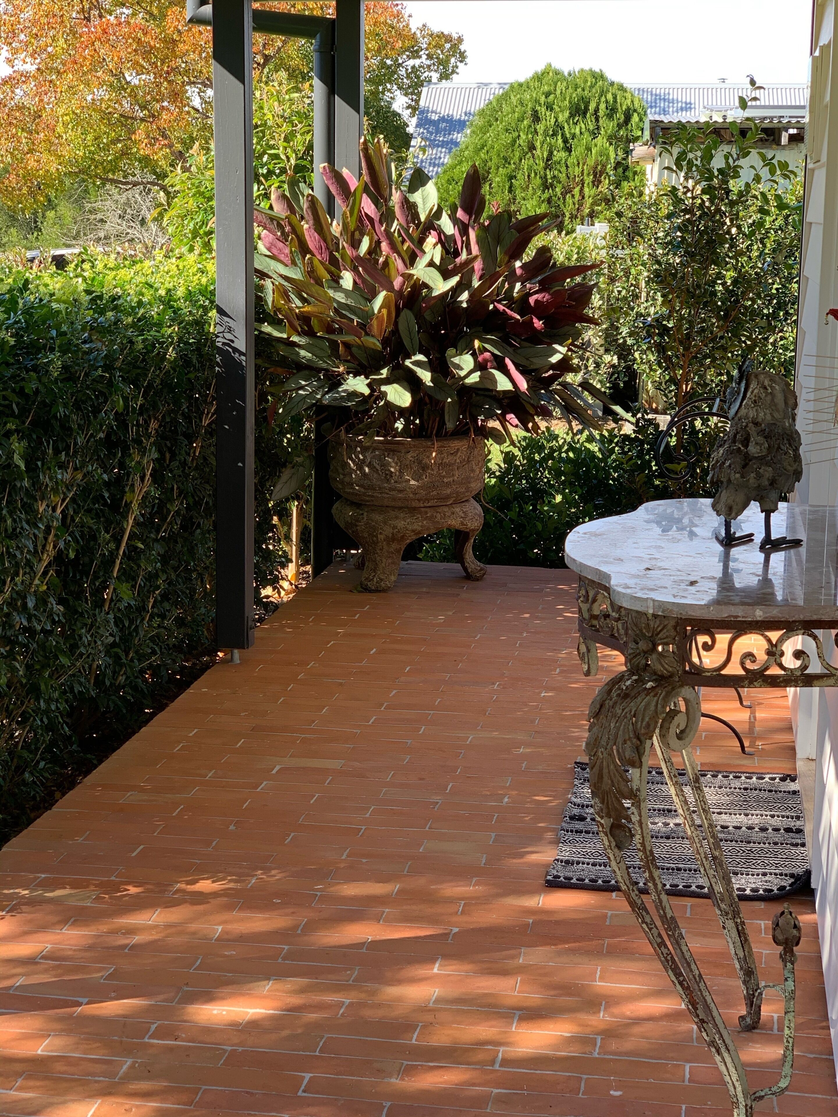 A paved pathway leading to a garden area with a large potted plant and a decorative table with a bird sculpture.