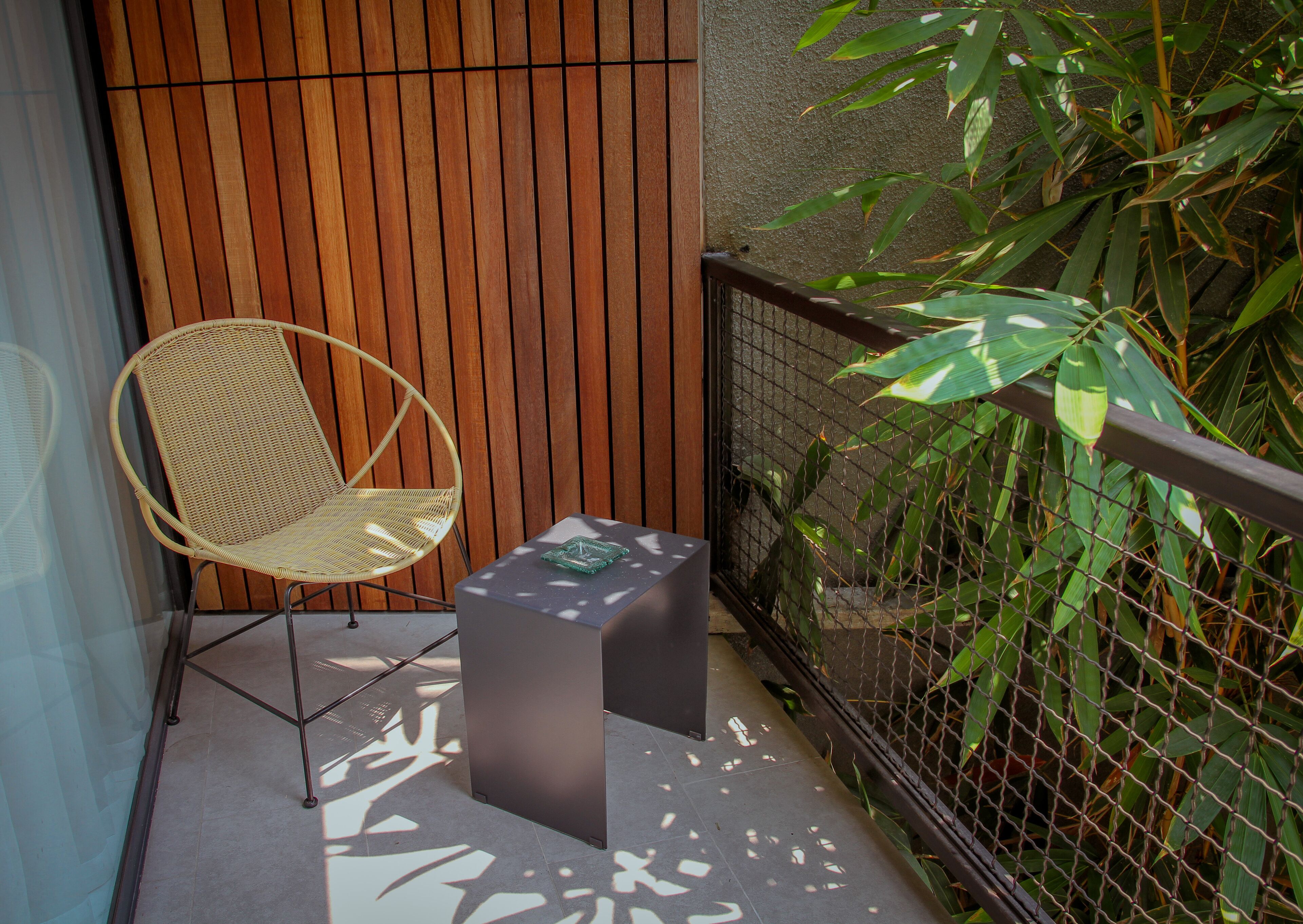 Un balcon avec un fauteuil en osier, une petite table et une plante en bambou.