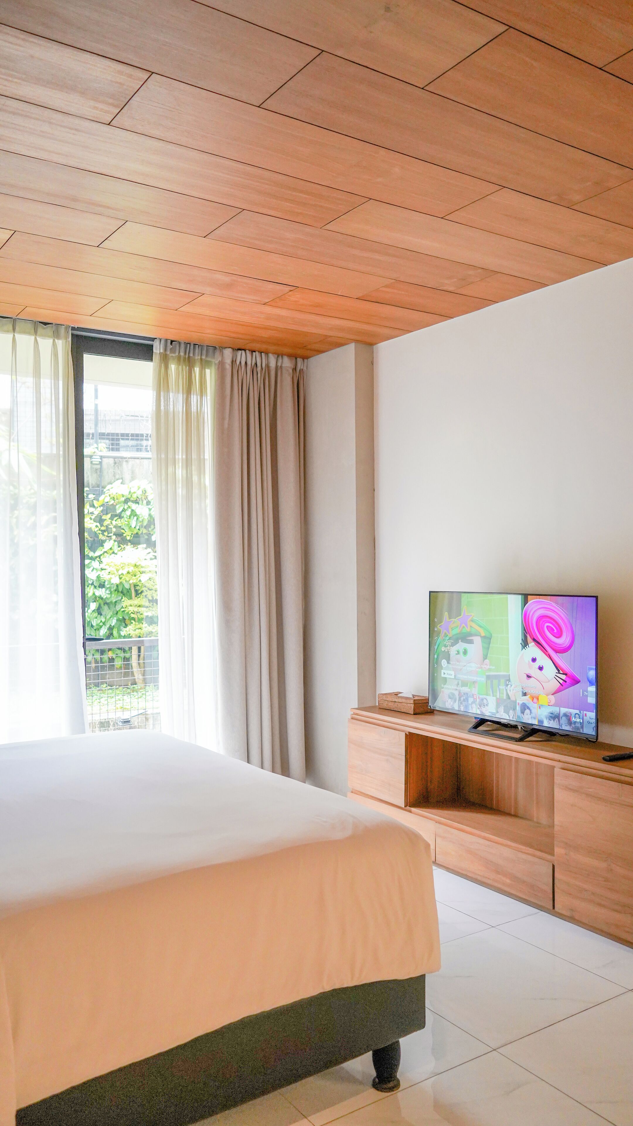 Camera d'albergo con un letto grande, soffitto in legno, una TV su un mobile in legno e una finestra con tende.