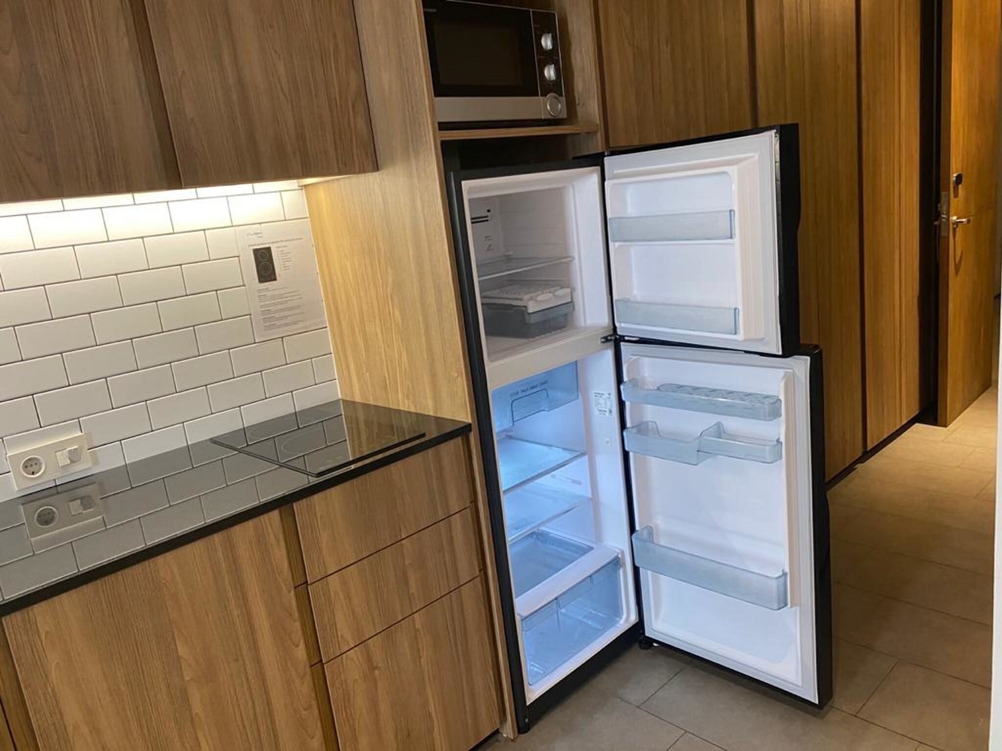 A kitchen with wooden cabinets, a microwave, and a double-door refrigerator.