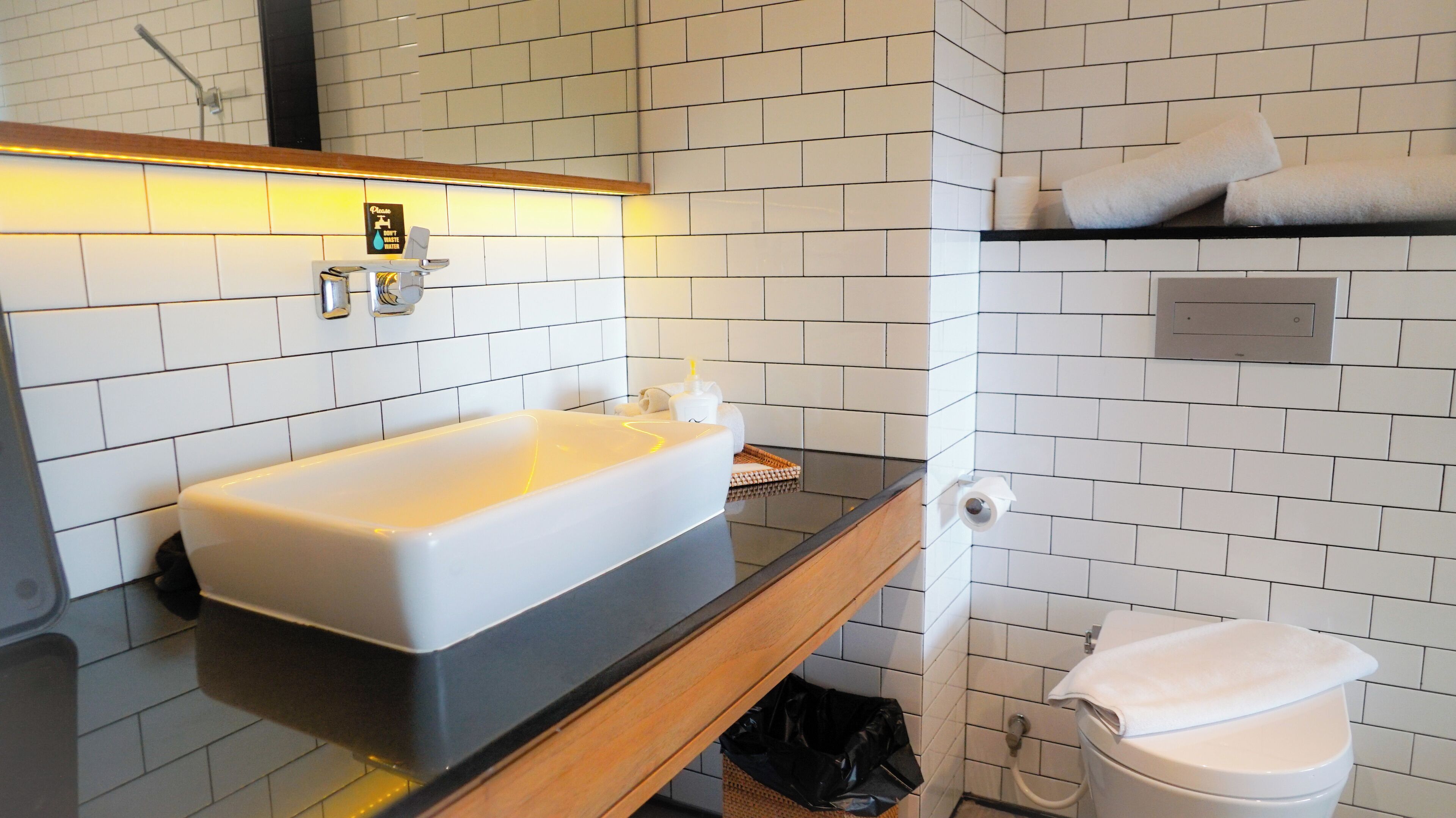 A modern bathroom with a white sink, black countertop, and white tiled walls.