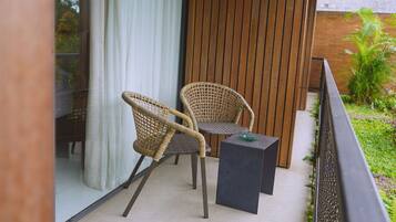 A balcony with wicker chairs and a small table, a wooden wall, and a glass door.