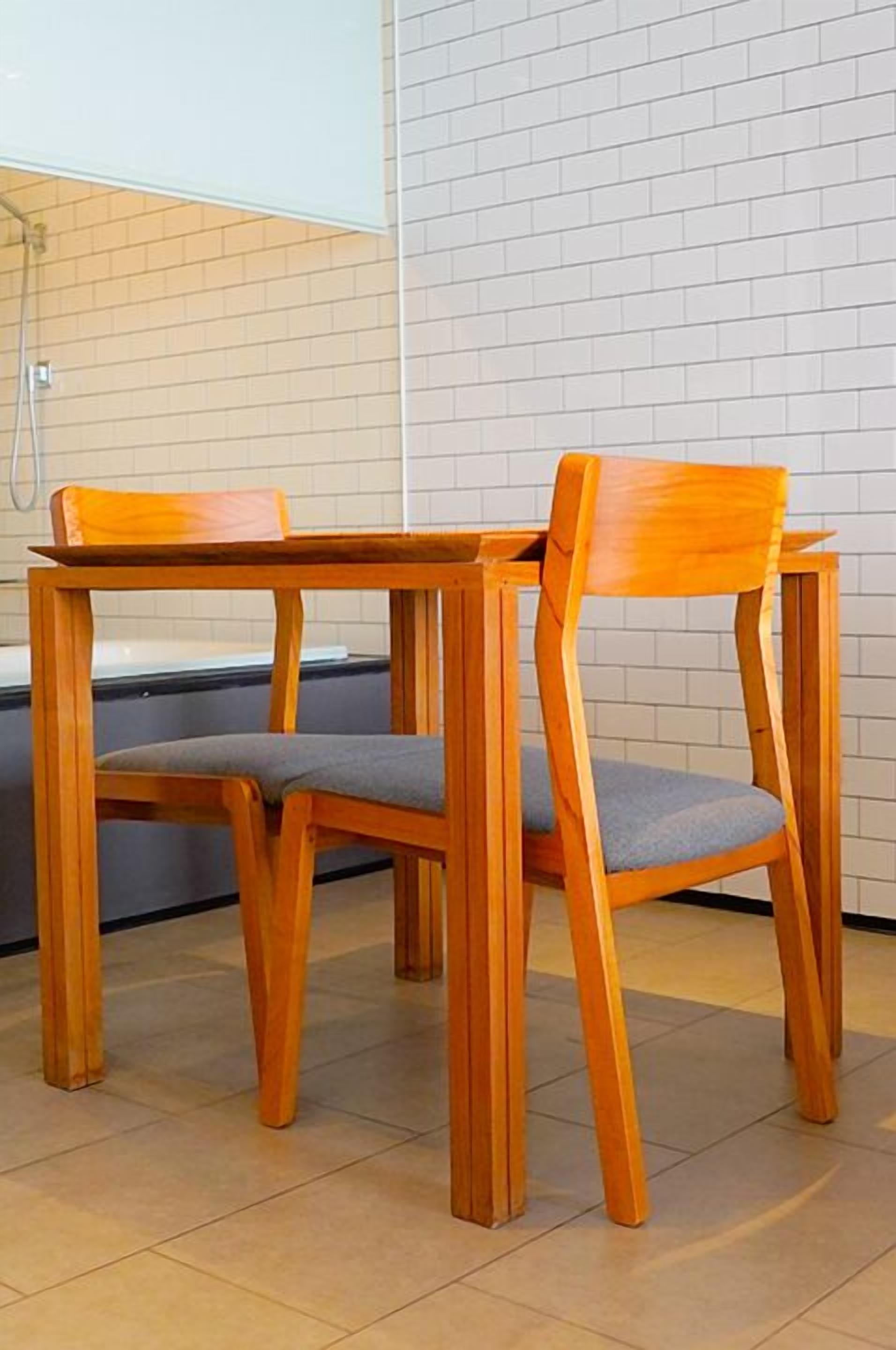 A wooden table and two chairs in a room with tiled walls and a bathtub in the background.