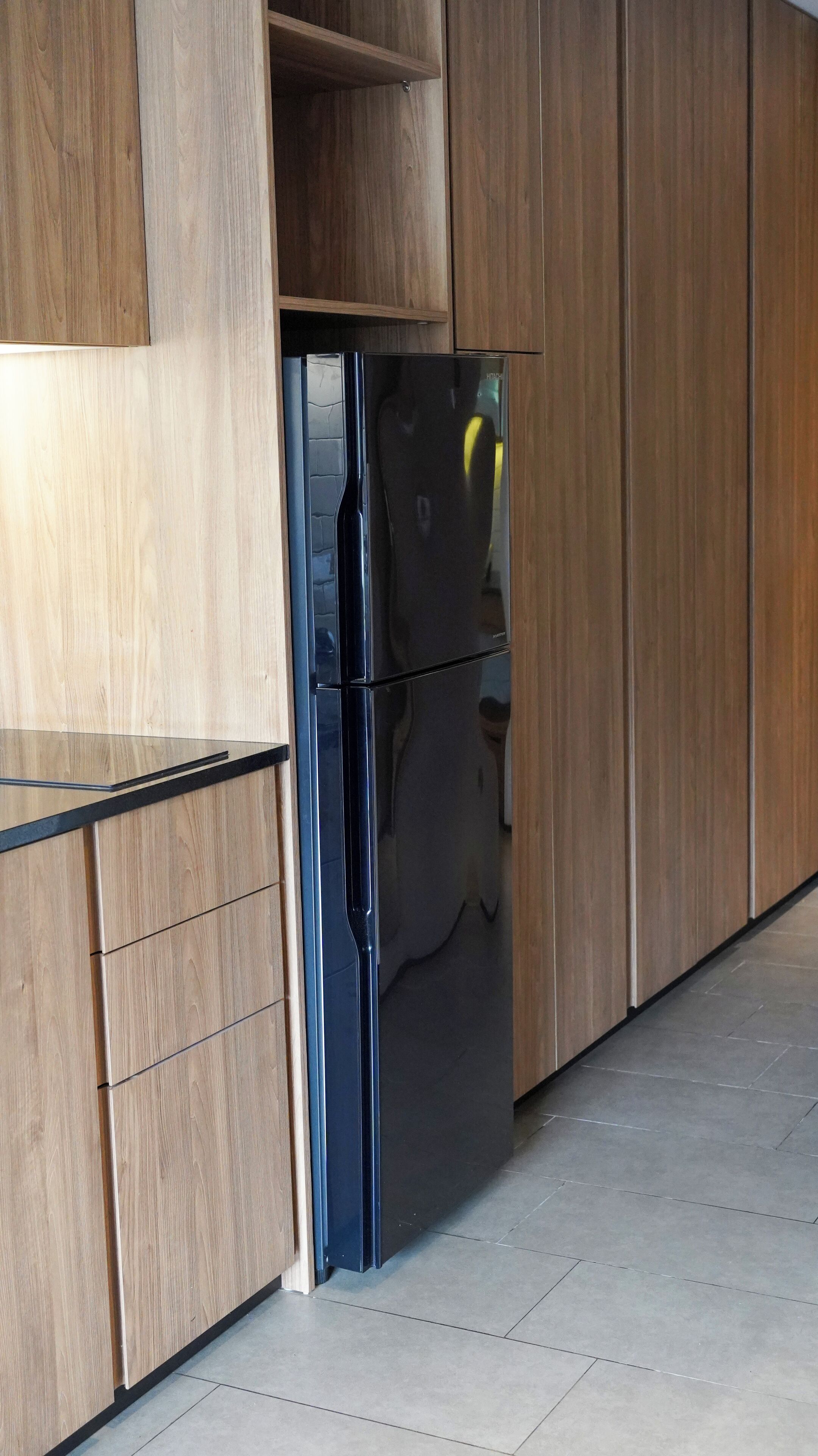 Une cuisine moderne avec des meubles en bois, un réfrigérateur noir et un plan de travail noir.