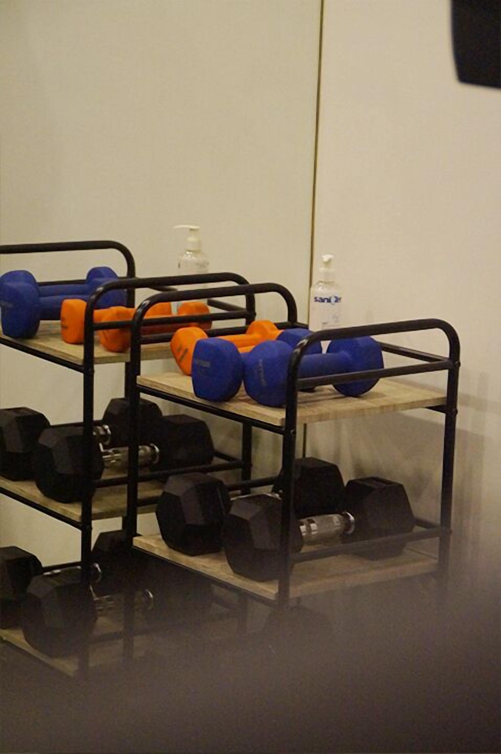A gym with weightlifting equipment including dumbbells and medicine balls on shelves.