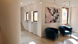 A spacious living room with a high ceiling, pendant lighting, a large abstract painting, and a staircase leading to another level. - Hotel Tari (Hoechberg)