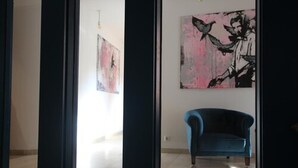 A room with a blue armchair, a large abstract painting on the wall, and a door leading to another room. - Hotel Tari (Hoechberg)