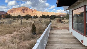 Une terrasse en bois avec une balustrade blanche, donnant sur un paysage aride et herbeux, avec une montagne en arrière-plan.