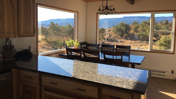 Une cuisine dotée de meubles en bois, d’un plan de travail en granit et offrant une vue sur un paysage montagneux grâce à de grandes fenêtres.