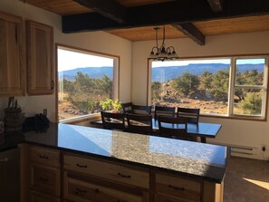 A kitchen with wooden cabinets, a granite countertop, and a view of a mountainous landscape through large windows.