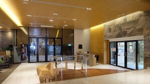 A modern lobby with a reception desk, seating area, and glass doors leading outside.
