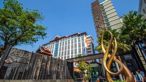 A hotel entrance with a prominent sign, a modern building in the background, and a large abstract sculpture.
